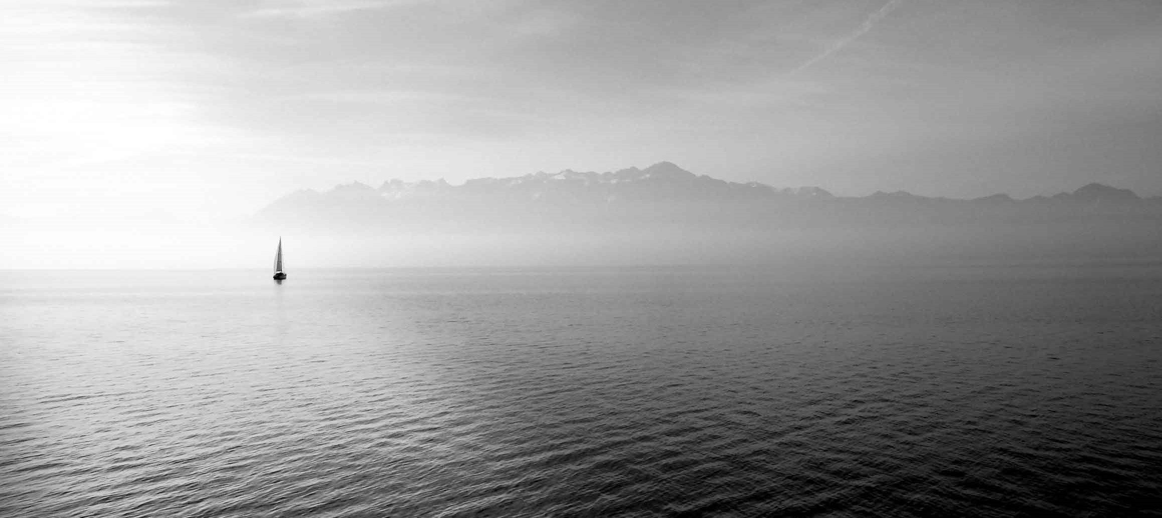 A small sailboat on a quiet lake, with mountains in the distance